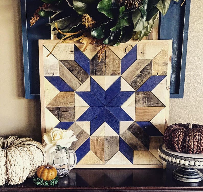 Puede incluir: Un tapiz de pared de madera con un patr&oacute;n geom&eacute;trico azul y marr&oacute;n. El patr&oacute;n est&aacute; formado por cuadrados y tri&aacute;ngulos, y crea una forma de estrella en el centro. El tapiz de pared est&aacute; enmarcado en madera y tiene un aspecto r&uacute;stico.