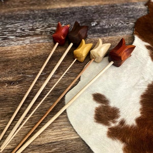 May include: Five wooden tulip-shaped flower picks in various colors, including red, brown, yellow, and natural wood. The picks are arranged on a wooden surface with a cowhide rug in the background.