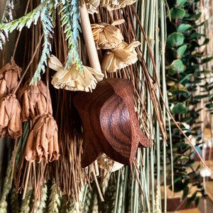 May include: A wooden star-shaped ornament with a brown finish, hanging from a dried floral arrangement. The arrangement includes dried flowers, grasses, and wheat.