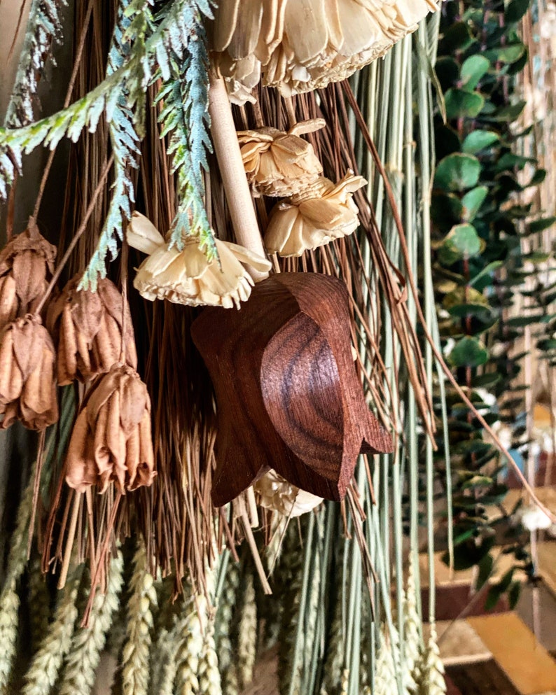 May include: A wooden star-shaped ornament with a brown finish, hanging from a dried floral arrangement. The arrangement includes dried flowers, grasses, and wheat.
