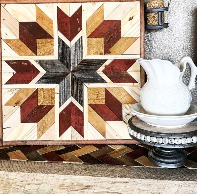 May include: A wooden wall art piece with a geometric pattern in shades of brown, red, and white. The art is framed and has a rustic look.