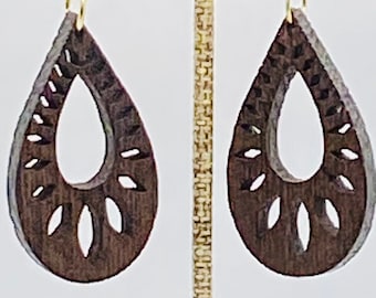 May include: A pair of dark brown wooden earrings with a teardrop shape and intricate cutouts. The earrings are hanging from gold hooks.