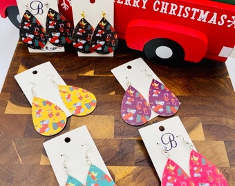 May include: A set of six pairs of teardrop-shaped dangle earrings with a Christmas theme. The earrings are made of leather and feature a variety of colorful patterns, including red, green, blue, yellow, and black. The earrings are displayed on a wooden surface with a white background.