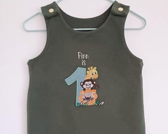 May include: A green sleeveless onesie with the text "Finn is 1" embroidered on the front. The number 1 is decorated with a giraffe, monkey, and lion.