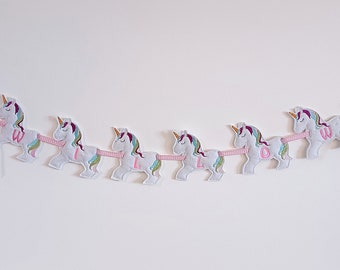 Könnte beinhalten: Ein weißer Filz-Einhorn-Banner mit rosa Buchstaben, die den Namen "WILLOW" buchstabieren. Jedes Einhorn hat eine Regenbogenmähne und einen Regenbogen-Schwanz.