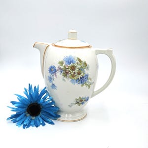 May include: White ceramic teapot with a floral design featuring blue and white flowers. The teapot has a gold trim around the lid and base.
