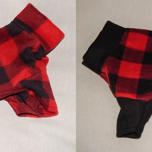 Op de afbeelding: Twee hondenjassen, elk met een rood-zwart buffelruitpatroon. Eén jas wordt van de zijkant getoond, de andere van bovenaf. De mouwen en de hals zijn zwart.