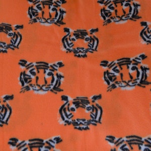 Op de afbeelding: Oranje stof met een herhalend patroon van zwarte en witte tijgergezichten.