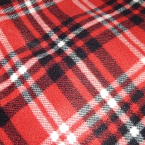 Op de afbeelding: Rood, zwart en wit geruite stof. Het patroon heeft een klassiek tartan ontwerp met elkaar kruisende lijnen die een rasterpatroon creëren. De stof heeft een zachte, getextureerde uitstraling, geschikt voor diverse textielprojecten.