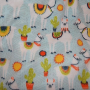 May include: A white fabric with a blue background featuring a repeating pattern of llamas, cacti, and suns. The llamas are white with colorful designs on their backs. The cacti are green with orange pots. The suns are yellow with orange rays.