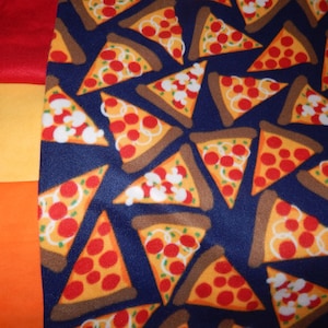 Op de afbeelding: Een blauwe stof met een herhalend patroon van pizzapunten. Elk punt is geel met rode pepperoni en witte kaas.