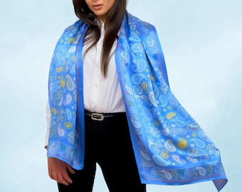 May include: A blue paisley patterned scarf with a white and yellow design. The scarf is draped around the neck of a person wearing a white shirt and black pants.