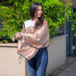 May include: A beige scarf with brown polka dots and a colorful border. The scarf is draped around a person's shoulders.
