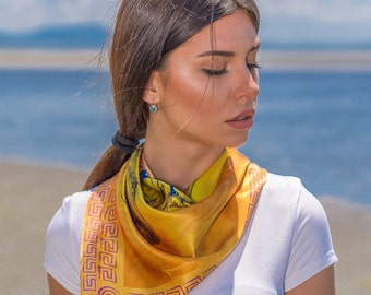 May include: A woman wearing a white t-shirt with a yellow silk scarf featuring a pink and purple geometric pattern around the edges. The scarf has a floral design in the centre.