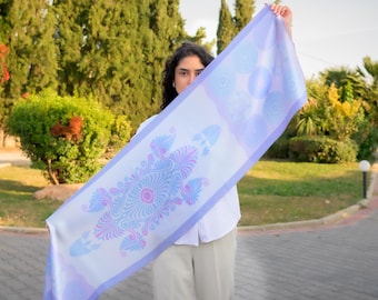 May include: A white silk scarf with a blue and pink floral design. The scarf is held up by a person in front of a green background.