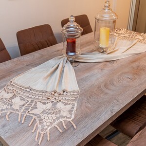 May include: A wooden dining table with brown chairs and a crocheted table runner with a fringe. Two glass jars with candles are on the table runner.