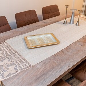 May include: A wooden dining table with a beige table runner and a crocheted lace trim. The table runner has a glass serving tray with four compartments in the center. There are four brown chairs around the table.