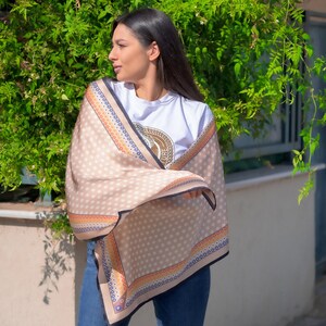 May include: A beige scarf with a black trim and a white polka dot pattern. The scarf has a colorful border with orange, blue, and red accents. The scarf is draped over a person's shoulders.