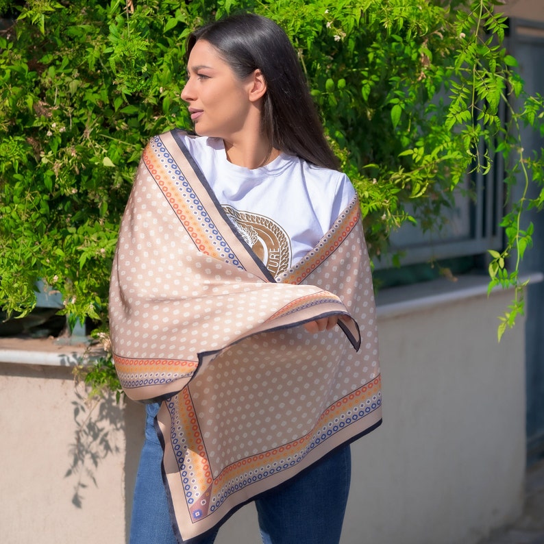 May include: A beige scarf with a black trim and a white polka dot pattern. The scarf has a colorful border with orange, blue, and red accents. The scarf is draped over a person's shoulders.