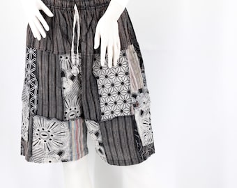 Pode incluir: Calções patchwork em tons de cinza, preto e branco, expostos em um manequim. Os calções apresentam cintura com cordão e uma variedade de padrões geométricos e florais. O tecido parece ser um material leve, adequado para climas quentes.