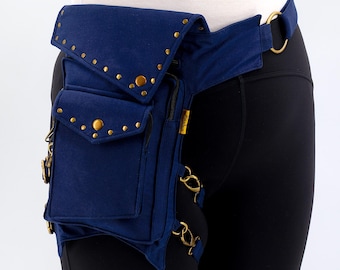 May include: A navy blue hip bag with multiple pockets and gold-colored rivets and hardware. The bag is worn around the waist and thigh, featuring a flap closure and adjustable straps. The bag is made of a durable fabric.