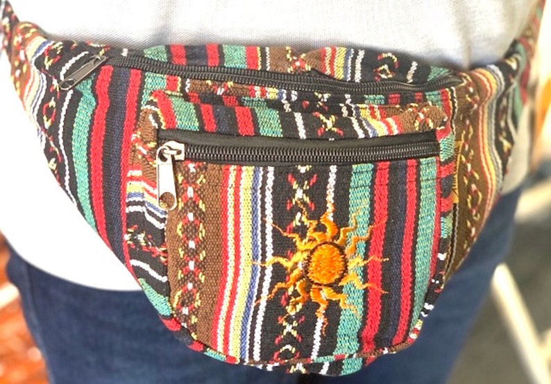 K&ouml;nnte beinhalten: Eine mehrfarbige, gestreifte Bauchtasche mit einem Rei&szlig;verschlussfach und einem gestickten Sonnendesign. Die Bauchtasche ist aus gewebtem Stoff und hat einen schwarzen Rei&szlig;verschluss.