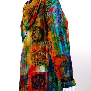 K&ouml;nnte beinhalten: Eine bunte Kapuzenjacke mit einem Batik-Muster und verschiedenen darauf gedruckten Symbolen. Die Jacke ist aus einem weichen, leichten Stoff gefertigt und hat eine lockere Passform.