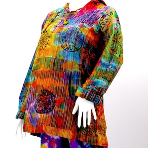 K&ouml;nnte beinhalten: Ein farbenfrohes Batik-Kapuzenoberteil mit Patchwork-Design, das verschiedene Symbole und Muster zeigt. Das Oberteil hat lange &Auml;rmel und eine lockere Passform.