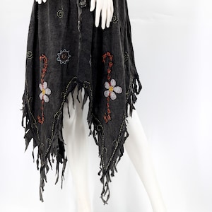 May include: A dark grey skirt with an elasticated waistband and drawstring. It features embroidered floral designs with orange and white accents. The hemline has a fringed edge, adding a bohemian flair to the garment.