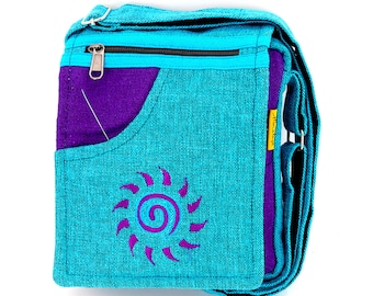 May include: A turquoise blue canvas crossbody bag with a purple pocket and a purple embroidered sun design. The bag has a zipper closure and an adjustable strap.