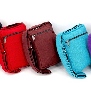 May include: Five canvas crossbody bags in different colors: black, red, brown, blue, and purple. The black bag has a tan pocket with a sun design.