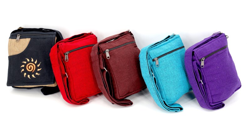 May include: Five canvas crossbody bags in different colors: black, red, brown, blue, and purple. The black bag has a tan pocket with a sun design.