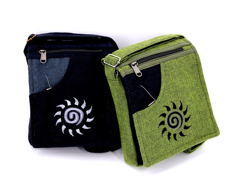 May include: Two canvas shoulder bags with a zippered closure and a pocket on the front. One bag is black with a white sun design and the other is green with a black sun design.