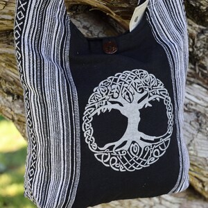 May include: Black and white striped tote bag with a white tree of life design on the front. The bag has a black strap and a button closure.