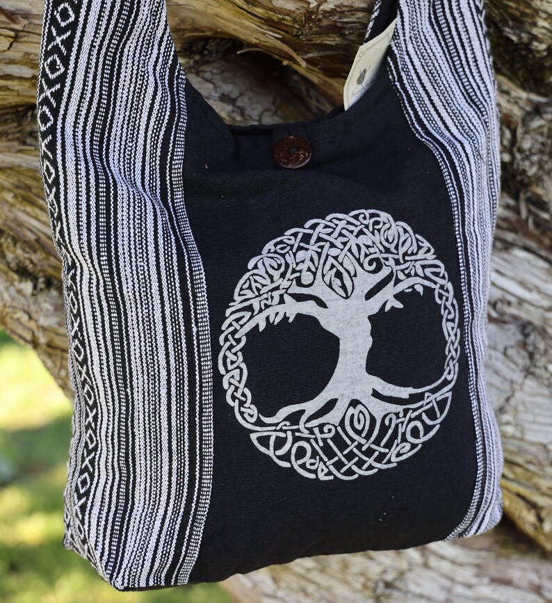 May include: Black and white striped tote bag with a white tree of life design on the front. The bag has a black strap and a button closure.