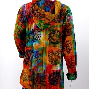 K&ouml;nnte beinhalten: Ein farbenfrohes Kapuzenhemd mit einem Batik-Muster und verschiedenen darauf gedruckten Symbolen. Die Symbole beinhalten eine Sonne, eine Blume und einen Kreis mit einem Stern darin. Das Hemd ist aus einem weichen, bequemen Stoff gefertigt und hat eine lockere Passform.