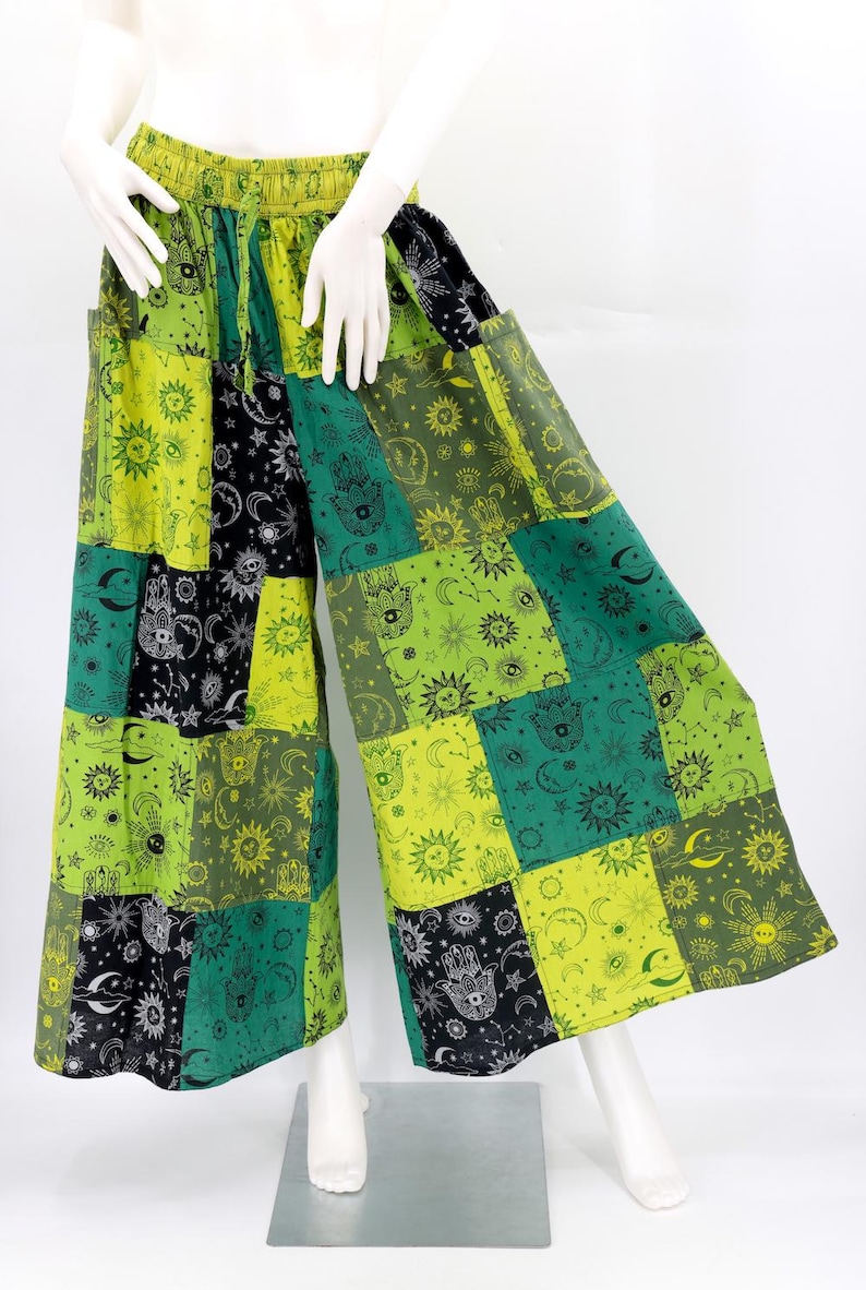 Puede incluir: Pantalones anchos de patchwork en tonos verdes, negros y amarillos. Los pantalones presentan un patr&oacute;n repetido de s&iacute;mbolos celestiales y de manos. La cintura es el&aacute;stica. Los pantalones se exhiben en un maniqu&iacute;.