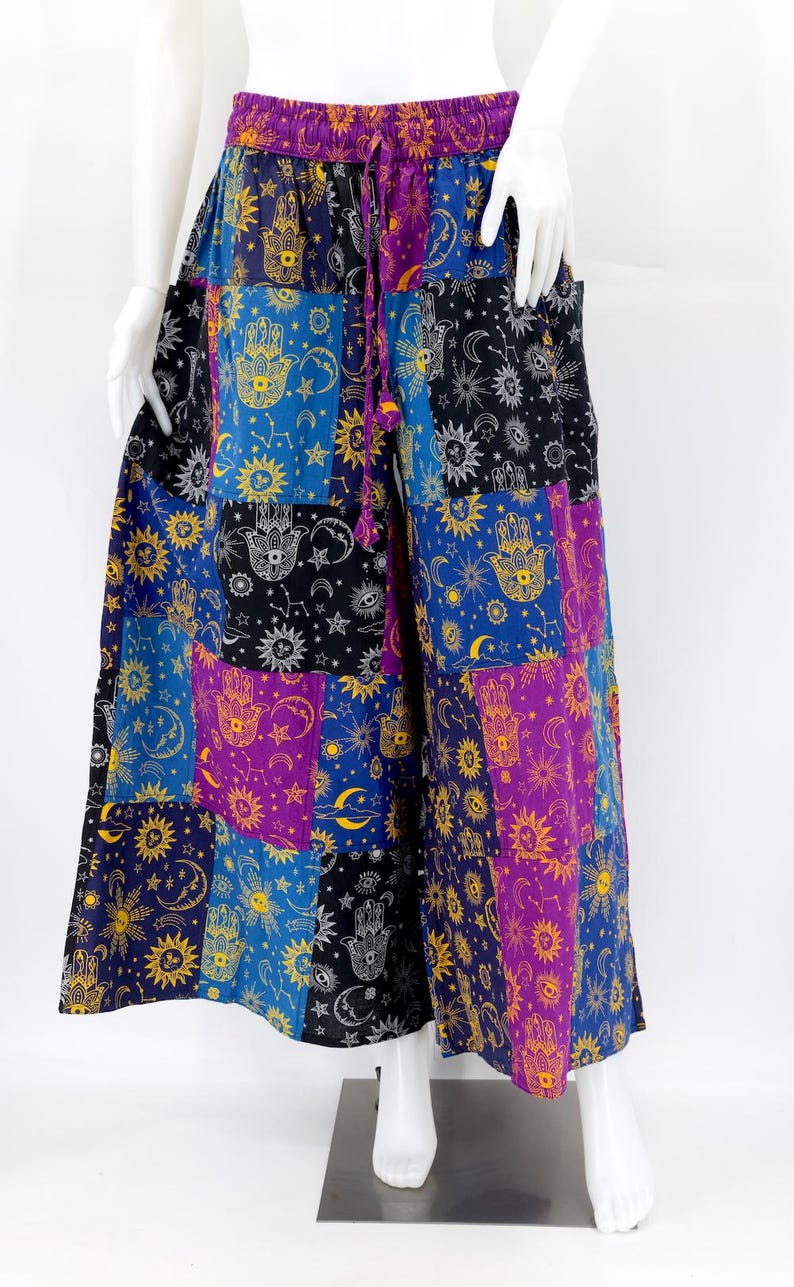 Puede incluir: Pantalones palazzo patchwork en tonos azules, morados, negros y amarillos. Los pantalones de pernera ancha presentan un estampado celestial y de mano de F&aacute;tima. La cintura tiene un cierre de cord&oacute;n. Los pantalones se exhiben en un maniqu&iacute;.
