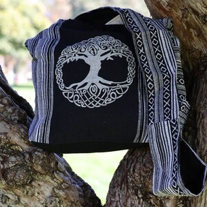 May include: Black and white canvas tote bag featuring a tree of life design. The bag has a long strap and is made from woven fabric.