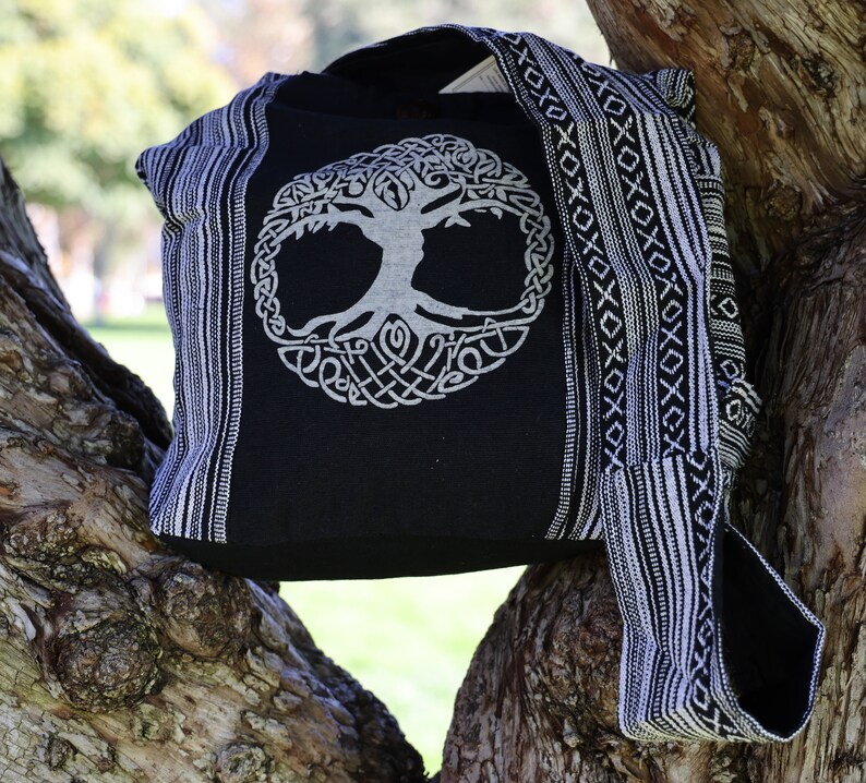 May include: Black and white canvas tote bag featuring a tree of life design. The bag has a long strap and is made from woven fabric.