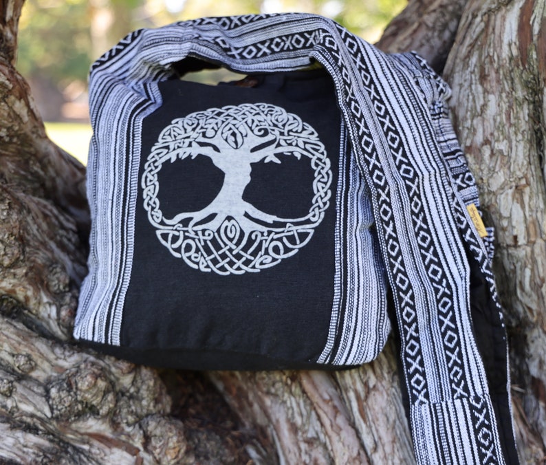 May include: Black canvas tote bag with a white tree of life design and a black and white striped strap.