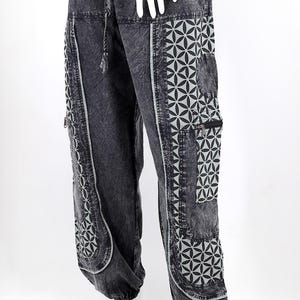 May include: Black denim pants with a geometric pattern on the sides. The pattern is a light gray color and features a flower of life design.