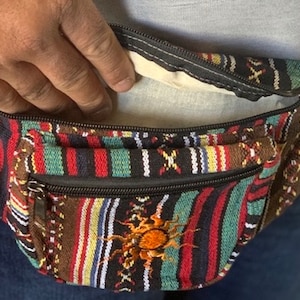K&ouml;nnte beinhalten: Eine mehrfarbige, gestreifte Bauchtasche mit einem Rei&szlig;verschlussfach und einem Sonnendesign. Die Bauchtasche ist aus gewebtem Stoff und hat einen schwarzen Rei&szlig;verschluss.