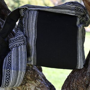 May include: A black and white striped fabric bag with a black canvas flap. The bag is hanging from a tree branch.