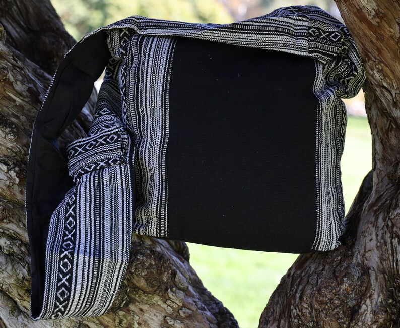 May include: A black and white striped fabric bag with a black canvas flap. The bag is hanging from a tree branch.