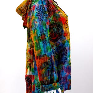 K&ouml;nnte beinhalten: Ein farbenfrohes Kapuzenhemd mit einem Batik-Muster und verschiedenen darauf gedruckten Symbolen. Das Hemd ist aus einem weichen, leichten Stoff gefertigt und hat eine lockere Passform.