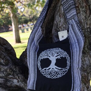 May include: Black and white cotton tote bag featuring a tree of life design. The bag has a long strap and is made from a soft, durable fabric.