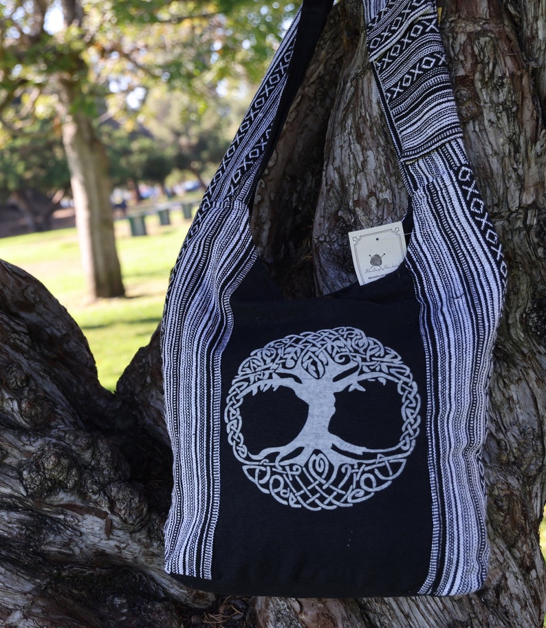 May include: Black and white cotton tote bag featuring a tree of life design. The bag has a long strap and is made from a soft, durable fabric.