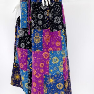Puede incluir: Falda larga de patchwork con dise&ntilde;o celestial y mano de F&aacute;tima. La falda tiene una cintura morada con cord&oacute;n y est&aacute; compuesta por cuadrados en tonos azules, morados, negros y dorados. La falda se exhibe en un maniqu&iacute;.