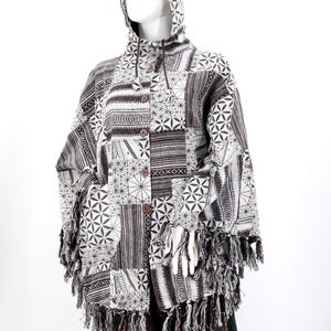 May include: A hooded patchwork jacket in shades of gray and white, featuring geometric and striped patterns. The jacket has a button-up front, pockets, and fringe trim along the hem and sleeves. The jacket is displayed on a mannequin.